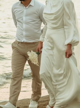 A couple walks by the sea in elegant attire, symbolizing love and togetherness.