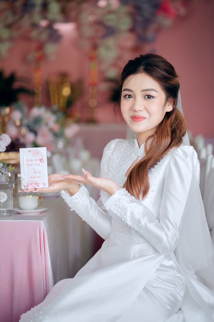 Young Brunette Woman Posing In Elegant White Dress By A Table