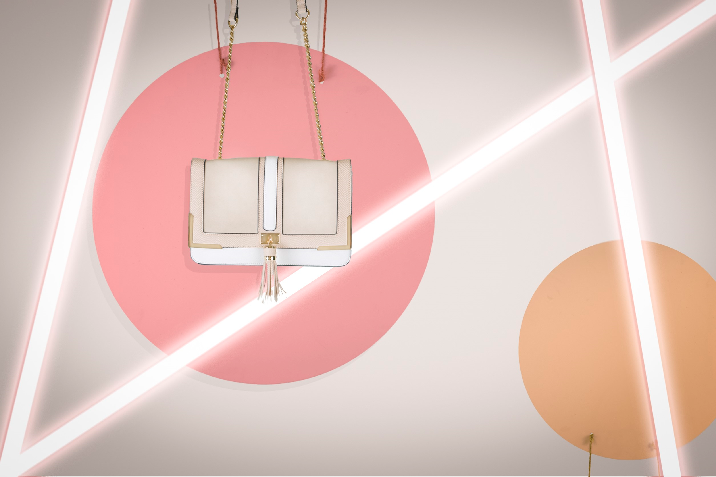 Elegant white handbag hanging against a pink and orange geometric background illuminated by neon lights.