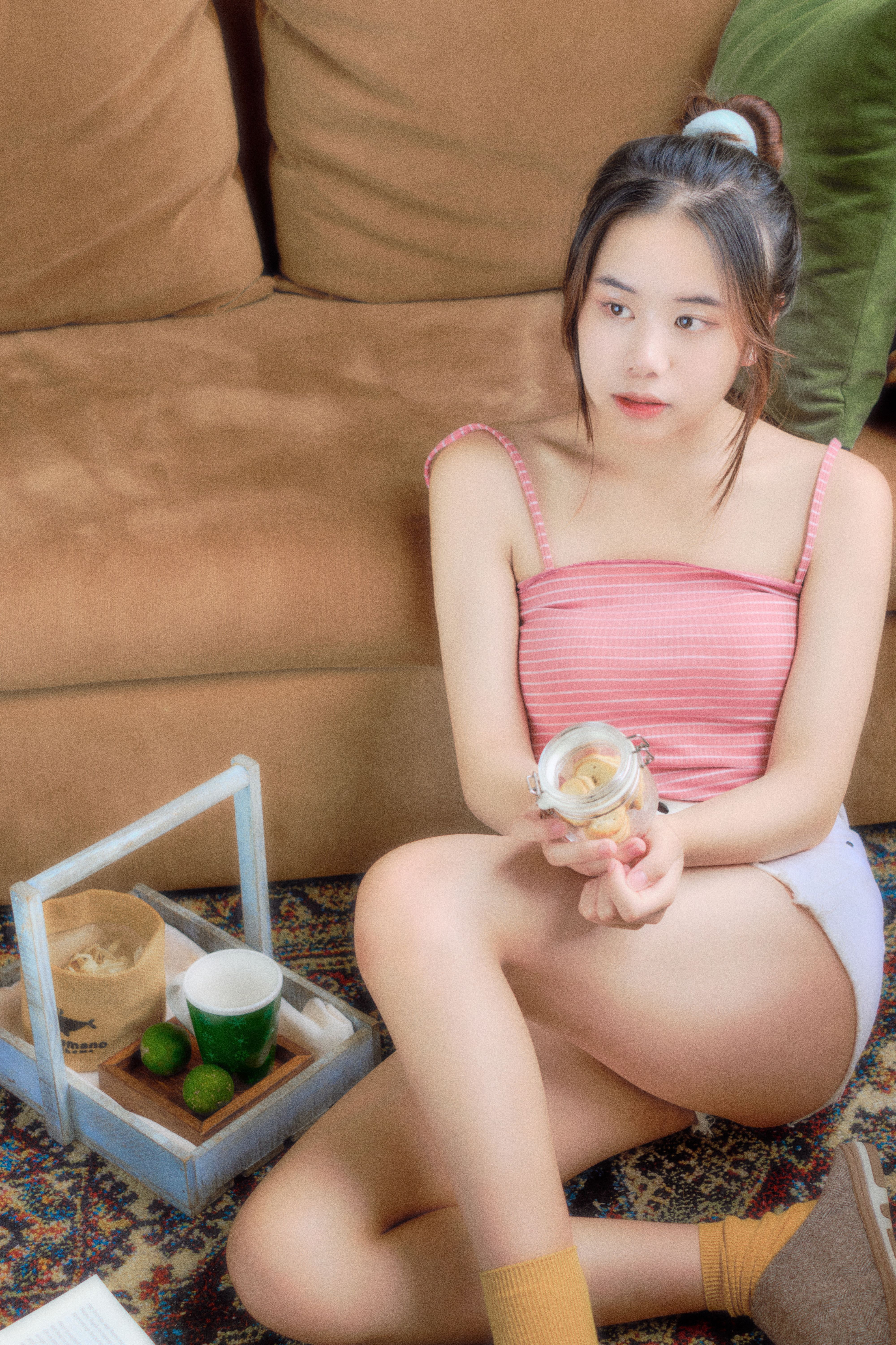 Young Asian woman enjoying a snack on the floor by a sofa, embodying casual indoor relaxation.