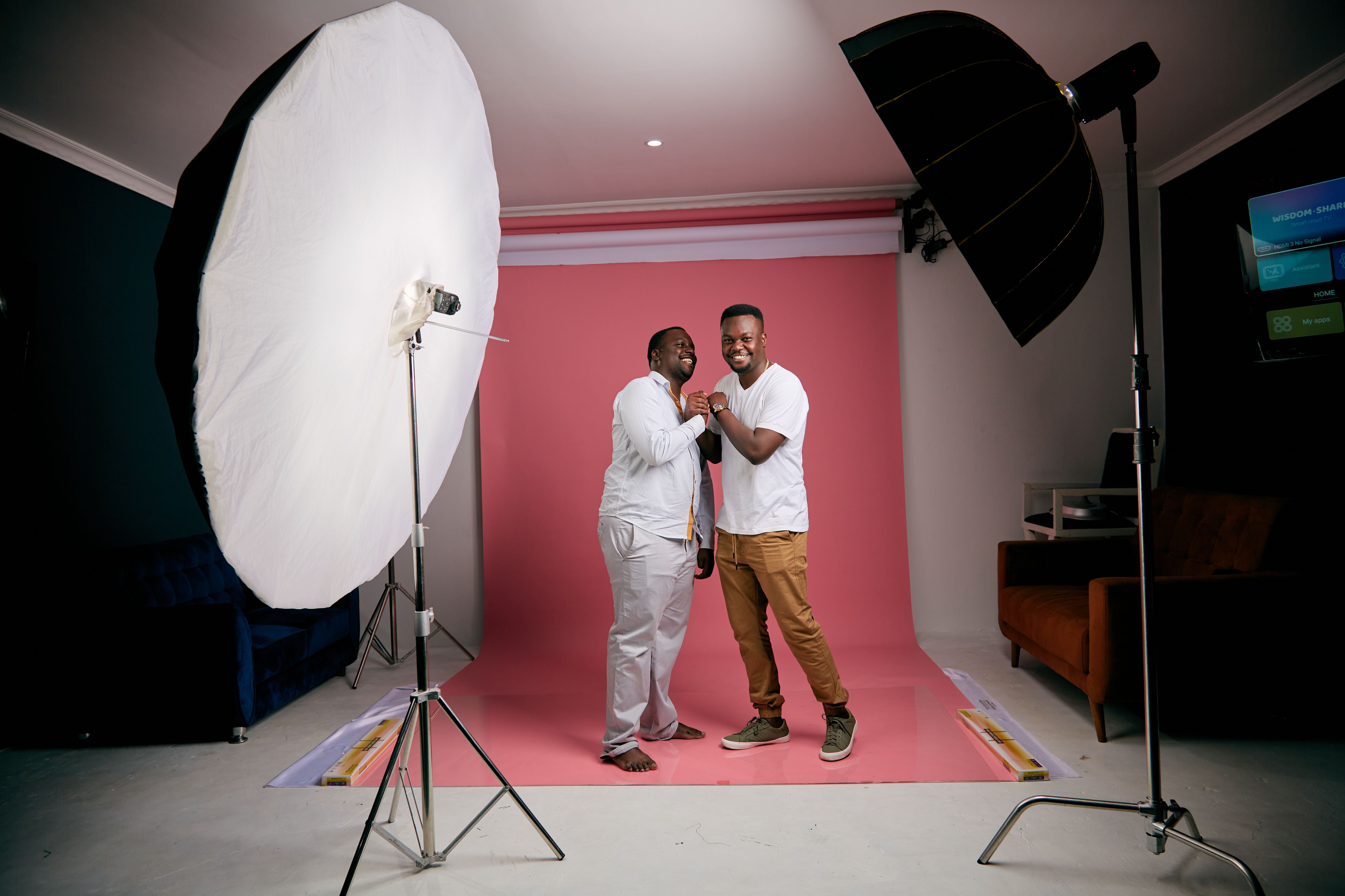 Two men happily posing with lighting equipment in a professional studio setup, showcasing a creative photoshoot.