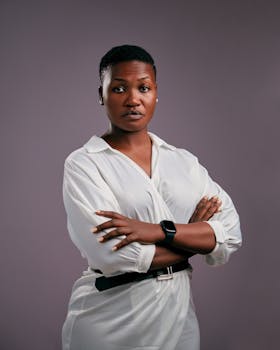 Confident woman with short hair standing with arms crossed in a studio portrait with gray background.