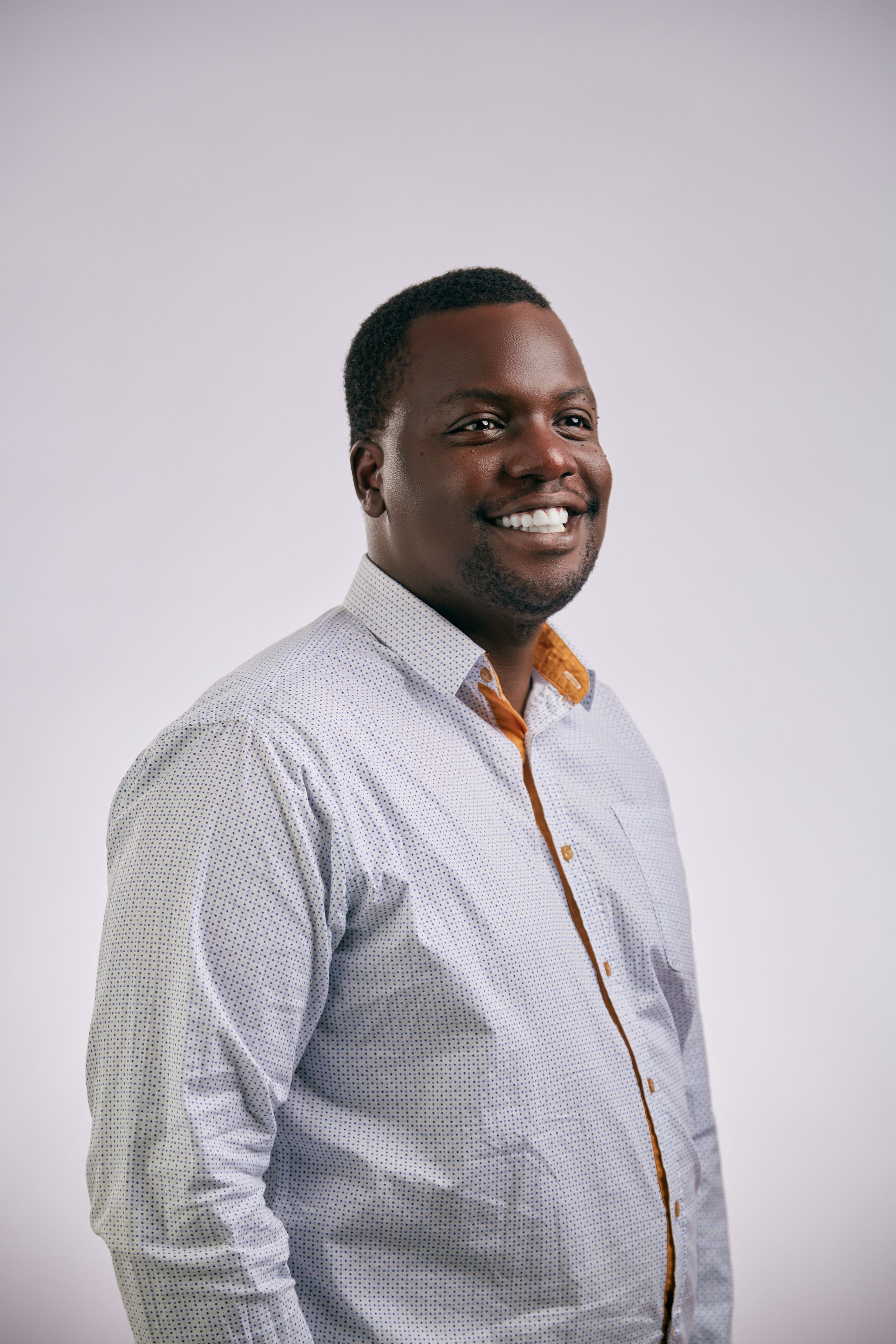 Portrait of a young smiling man in a patterned shirt against a grey studio background.