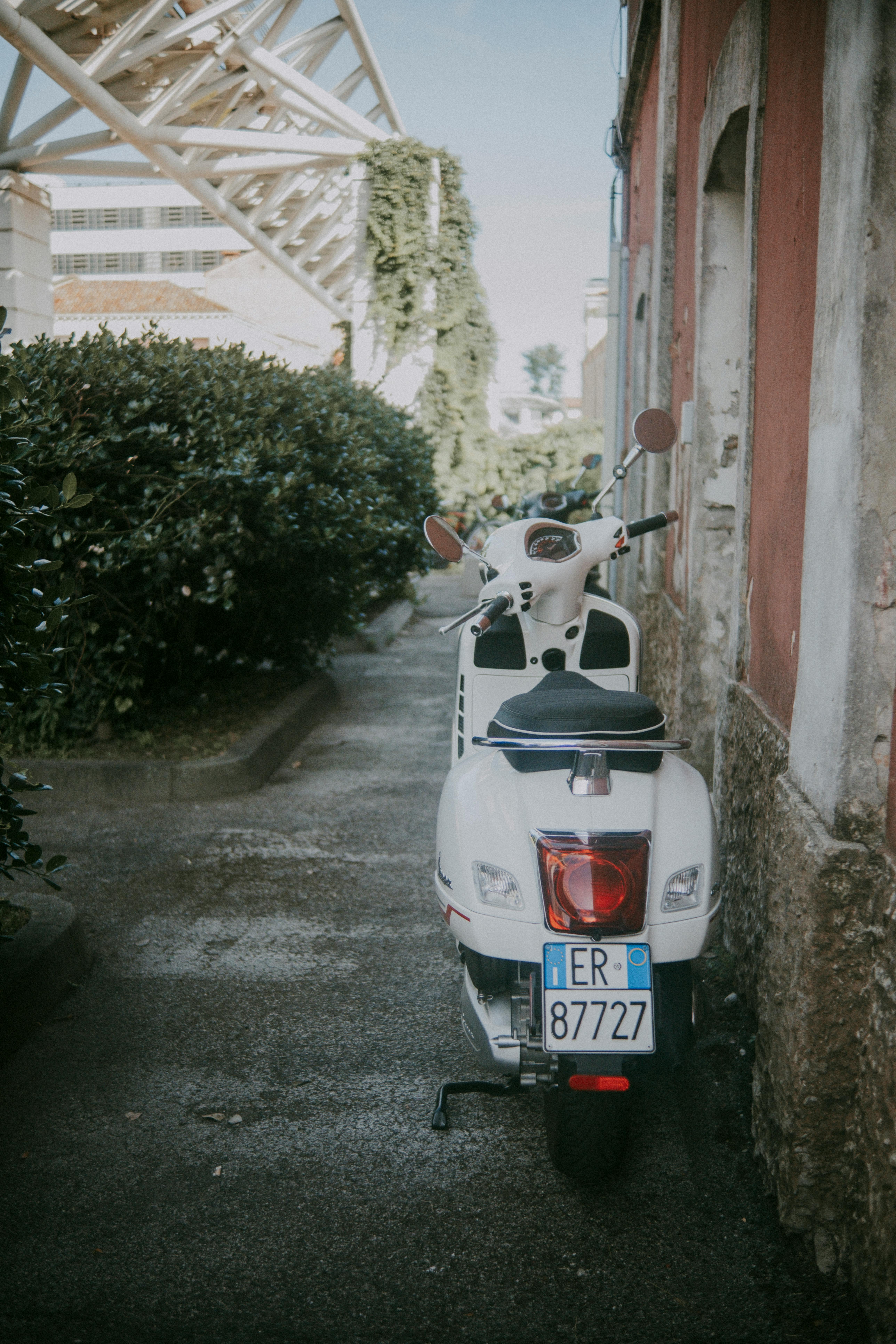 A white scooter parked in a narrow urban alleyway next to residential buildings.
