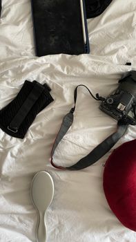 A camera, tablet, and hairbrush arranged on a white bed for a creative workspace setup.