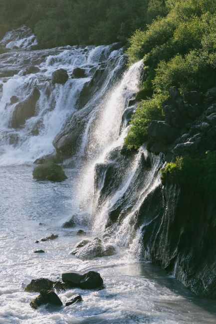 Majestic waterfall flowing through rocky terrain surrounded by lush greenery in Iceland.