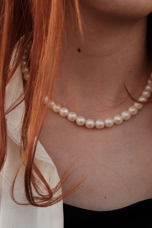 Free Close-up of a woman's neck with red hair and a pearl necklace. Perfect for fashion and jewelry stock images. Stock Photo