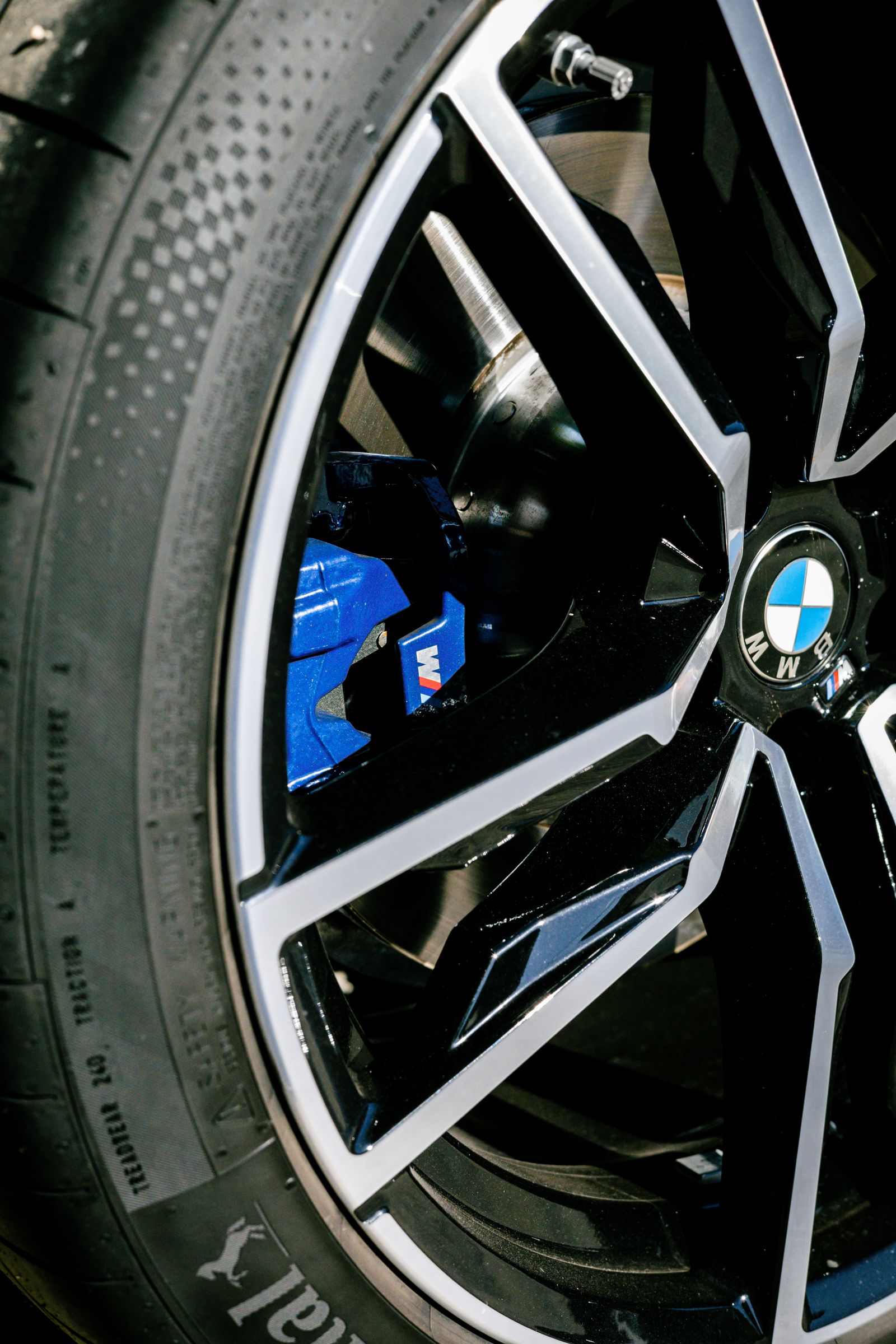 Close-up of a BMW performance wheel, tire, and brake caliper illustrating suspension geometry at the corner of the car