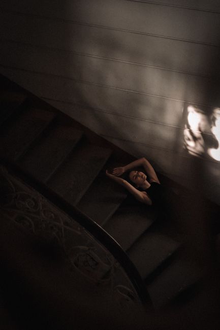 Artistic top view of a woman posing on a dimly lit staircase, adding drama and mystery.