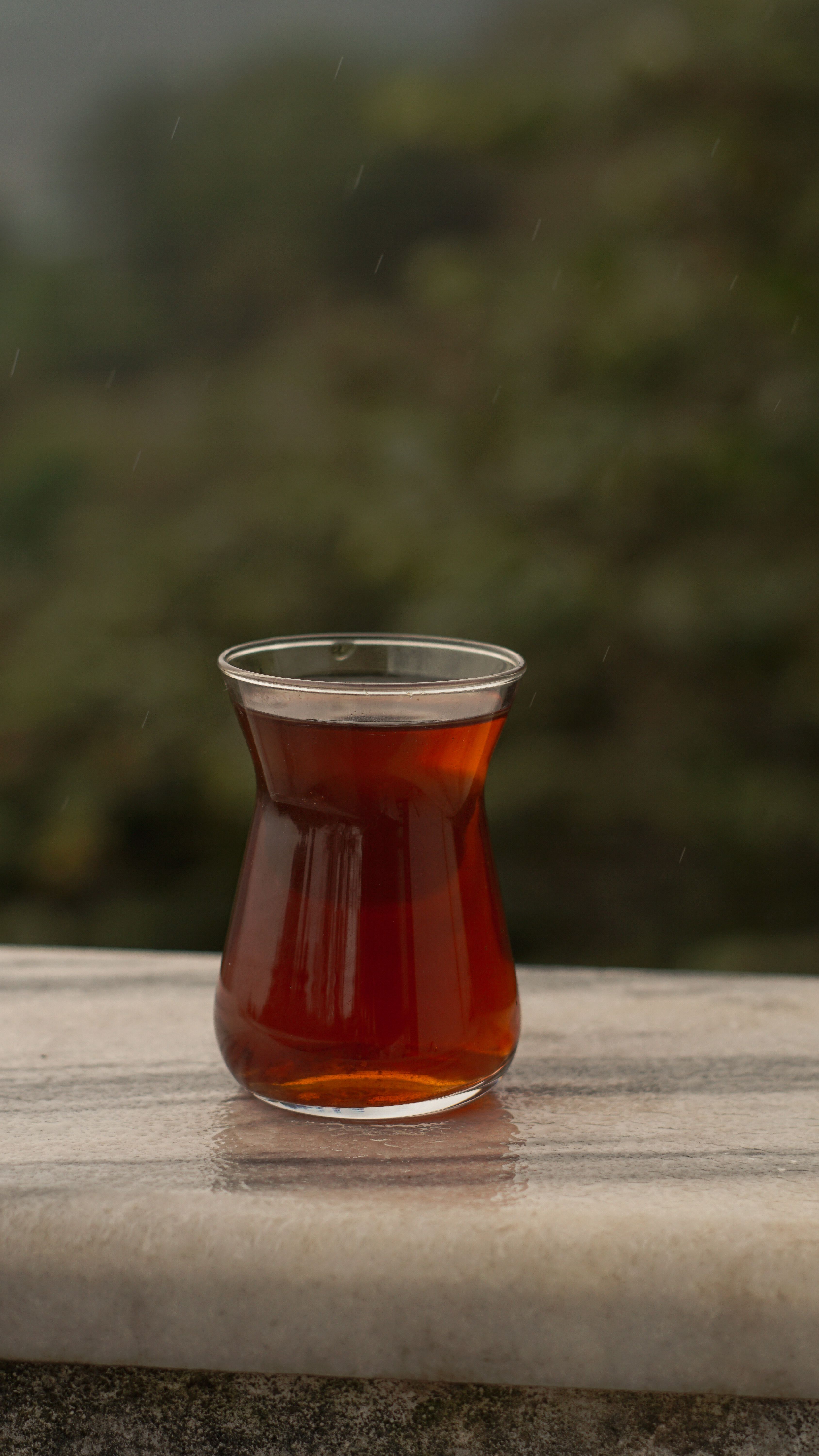 A steaming cup of Turkish tea in an iconic glass, set against a serene outdoor backdrop.