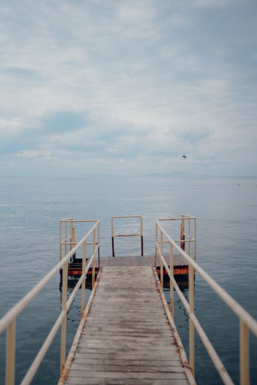 Free Serene view of a wooden pier extending into a calm sea under a cloudy sky, evoking a sense of peace. Stock Photo