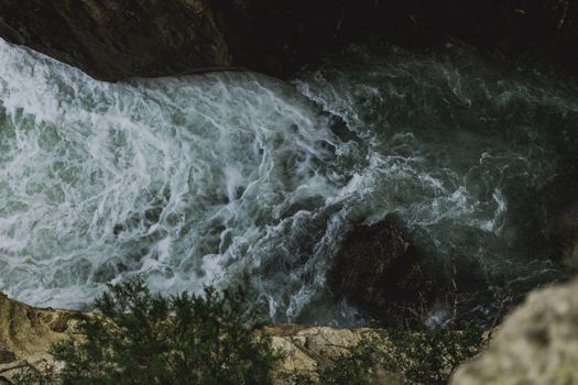 Dramatic aerial view of fast-flowing river through rugged mountain gorge with lush greenery.