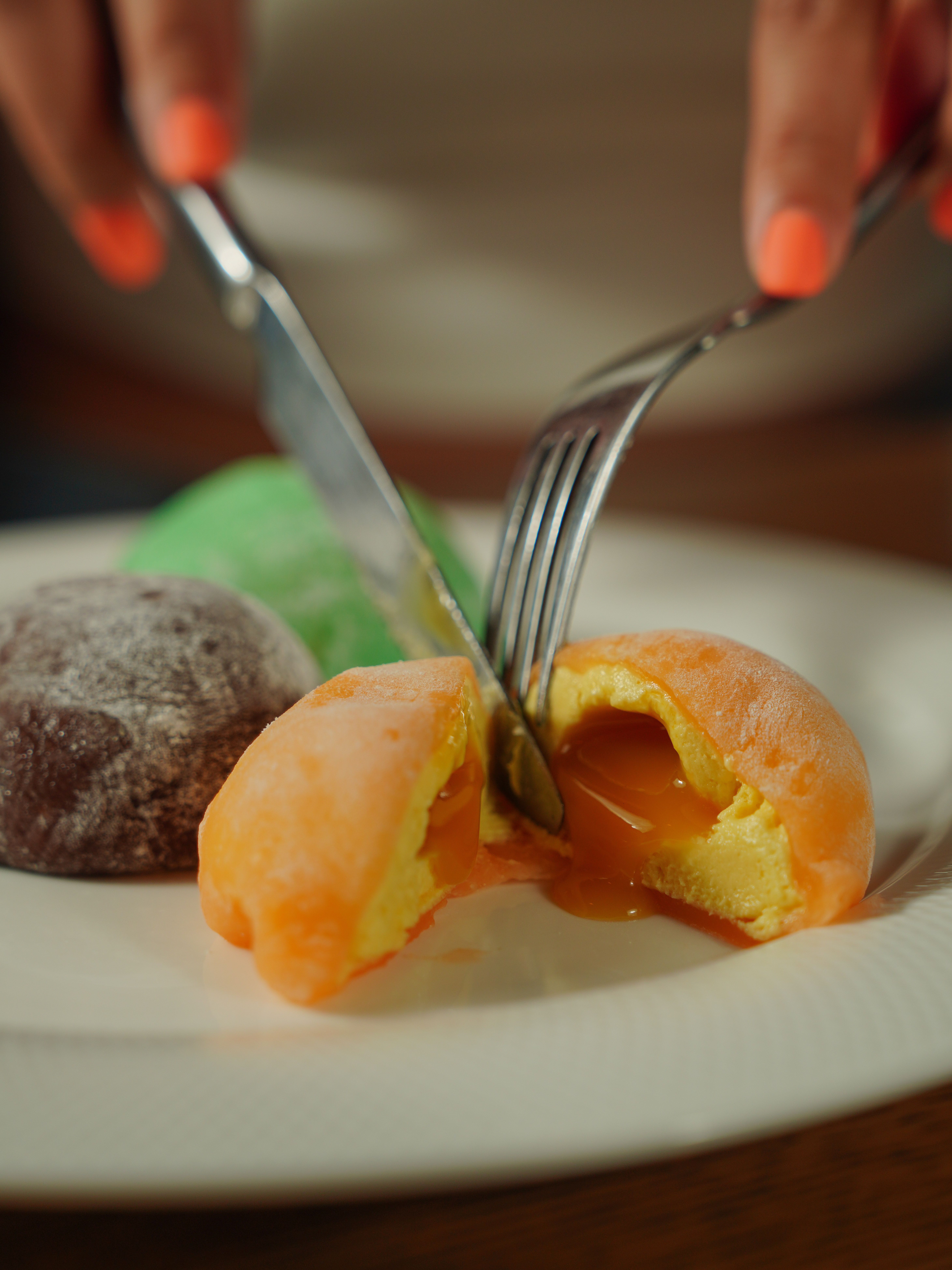 Delicious mochi being sliced open to reveal a creamy filling, served on a white plate.