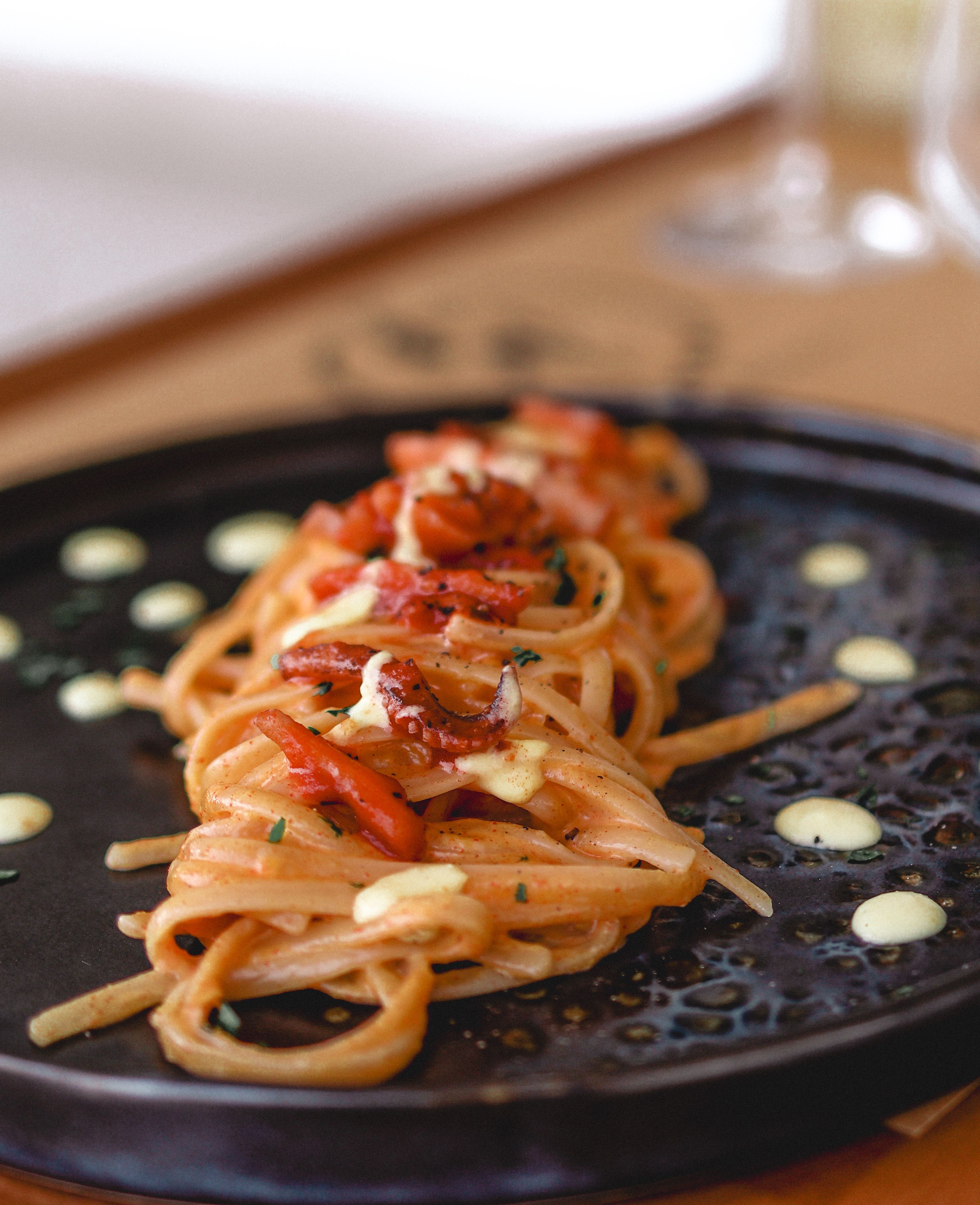 A close-up shot of creamy pasta with tomatoes and herbs beautifully presented on a black plate.