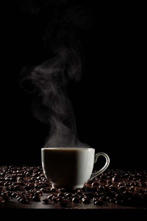 Free A steaming cup of coffee surrounded by beans on a dark background, creating a warm, inviting mood. Stock Photo
