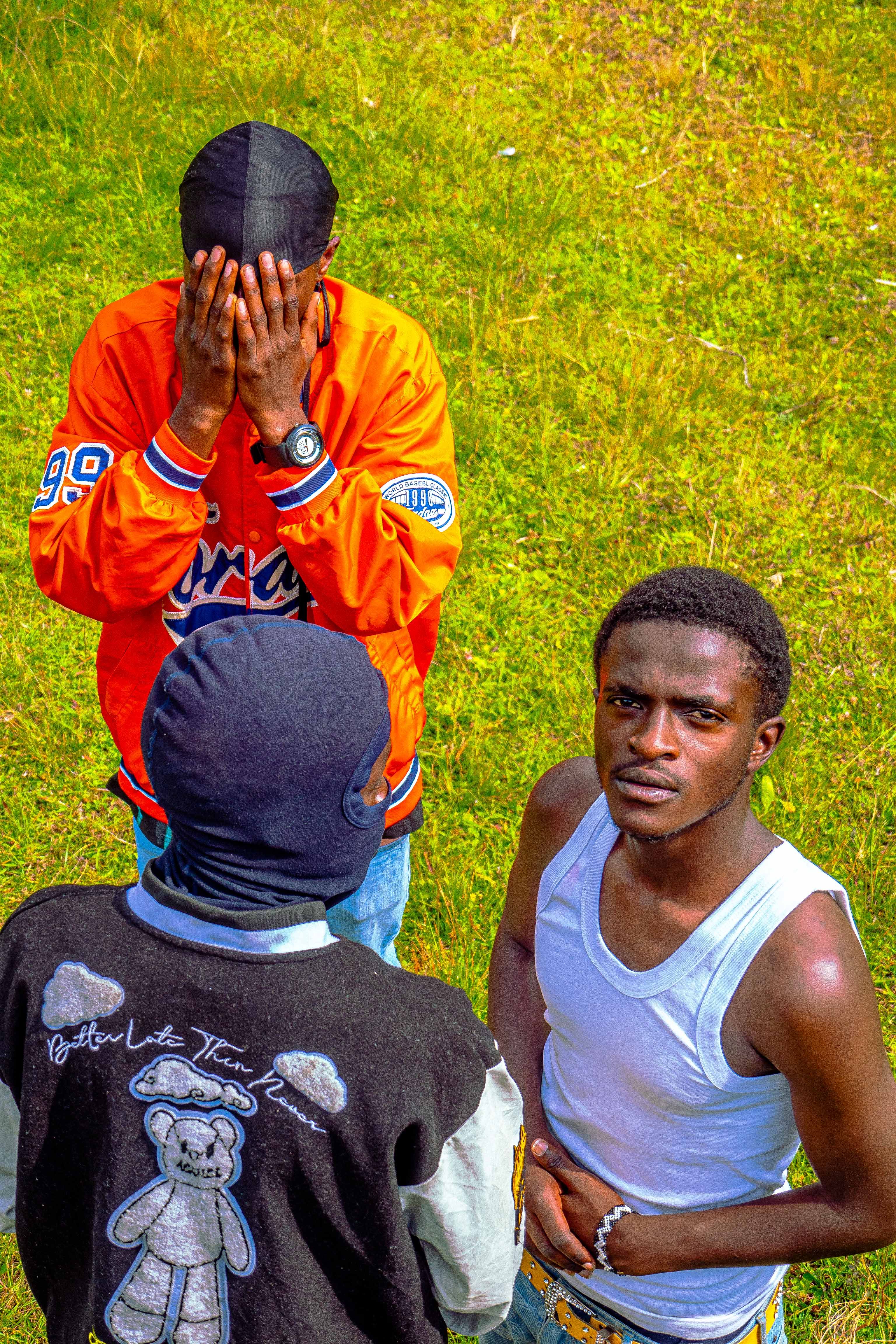 Three young men interact in a sunny outdoor field, depicting casual and vibrant style.