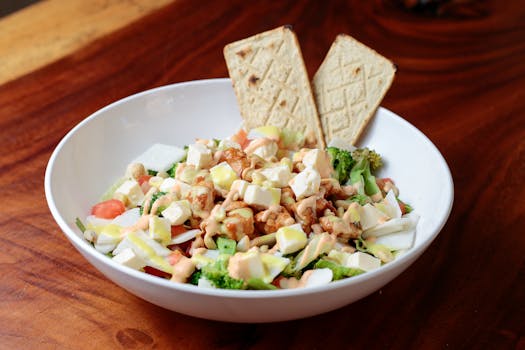 Vibrant fresh salad topped with walnuts, cheese, and crispy bread sticks in a white bowl on a wooden table.