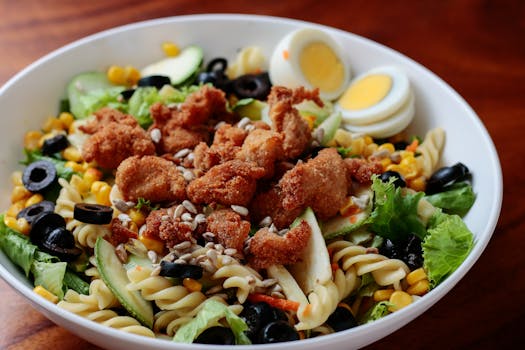 Delectable crispy chicken pasta salad with fresh vegetables and boiled eggs, perfect for a hearty meal.