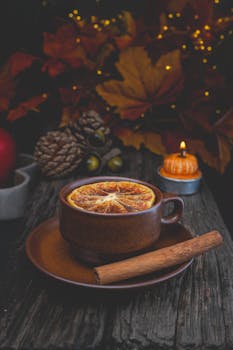 Warm autumn scene with spiced tea, orange slice, and cinnamon stick on rustic table.