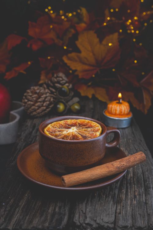 Free Warm autumn scene with spiced tea, orange slice, and cinnamon stick on rustic table. Stock Photo
