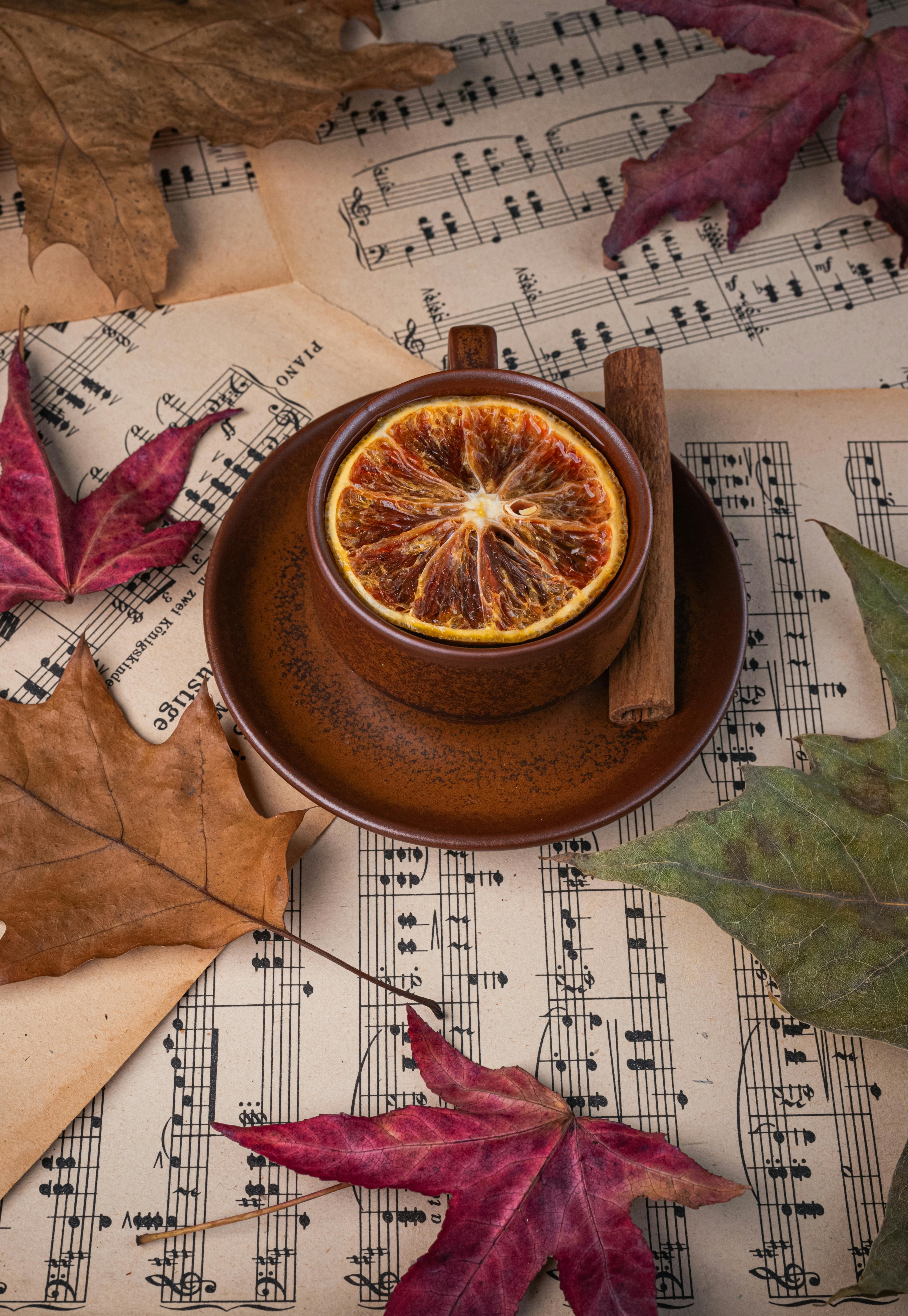 Warm autumn setup with tea, dried lemon, cinnamon, and autumn leaves on sheet music.