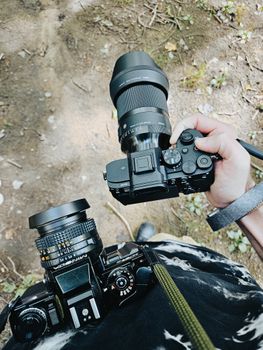 Photographer holding two cameras outdoors capturing nature moments.