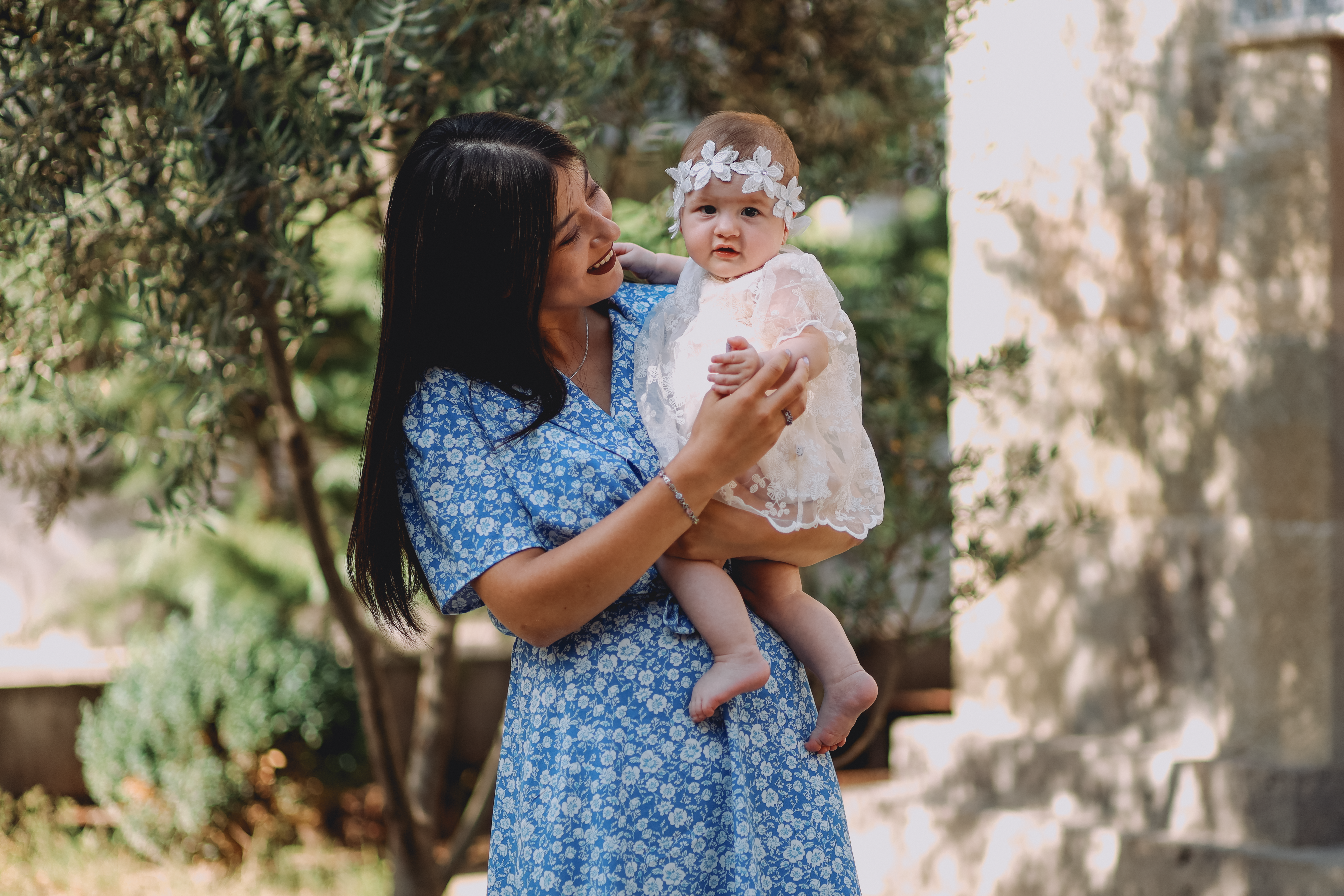 A mother joyfully holding her baby in a floral dress under the sun.