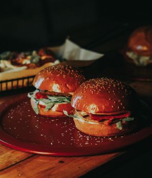 Two gourmet burgers with lettuce and tomatoes on a wooden table. Perfect for fast food enthusiasts.