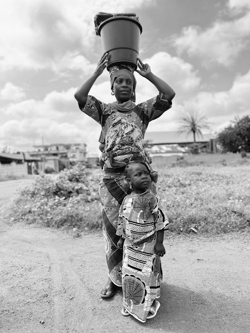 Daughter and Mother with a Bucket on her Head Standing on a Street