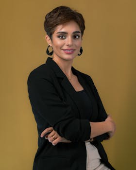 Portrait of a confident businesswoman in black jacket with a warm smile, set against a neutral background.