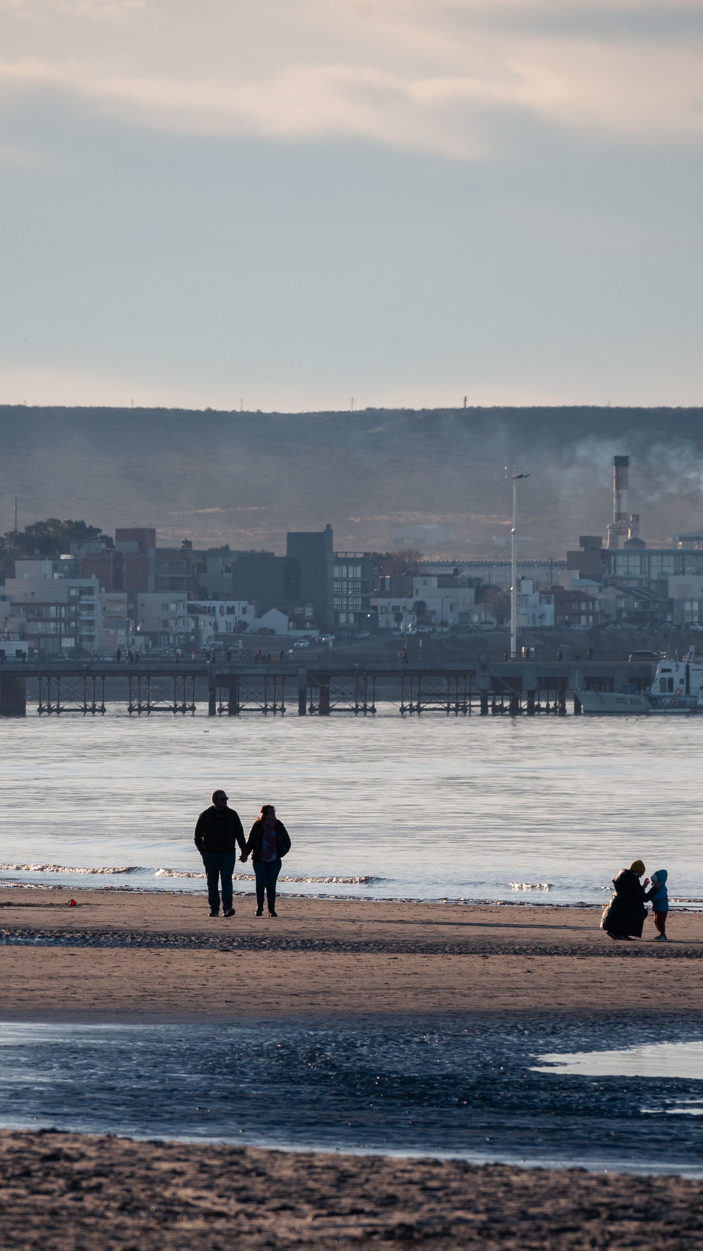 A serene beach walk with people and city skyline in the background during sunset.