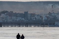 A serene beach walk with people and city skyline in the background during sunset.