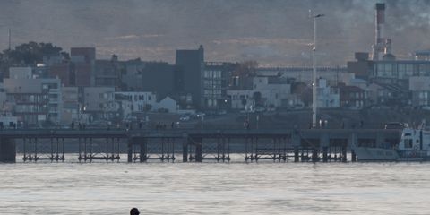A serene beach walk with people and city skyline in the background during sunset.