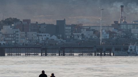 A serene beach walk with people and city skyline in the background during sunset.