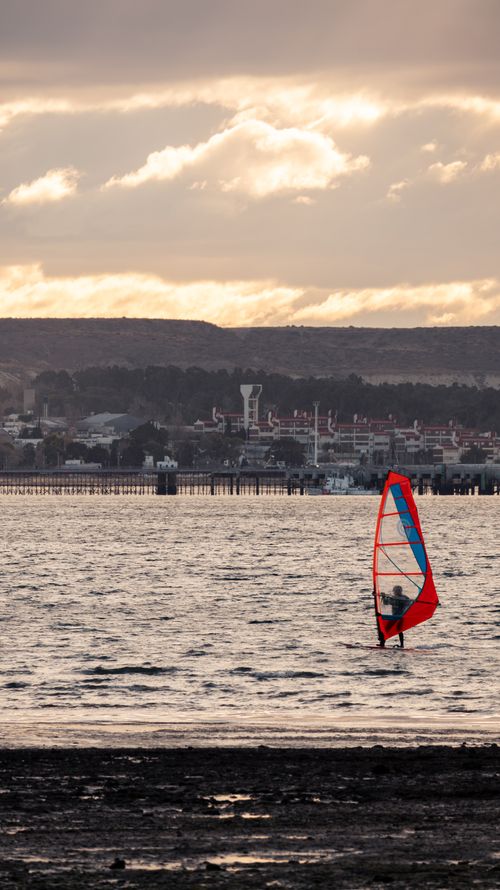Free A windsurfer glides near the shore under a dramatic sunset sky. Stock Photo