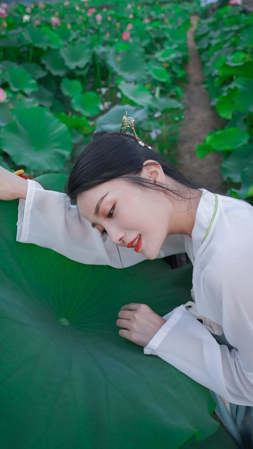 Free Asian woman in traditional attire leaning on a lotus leaf in a vibrant green field. Stock Photo