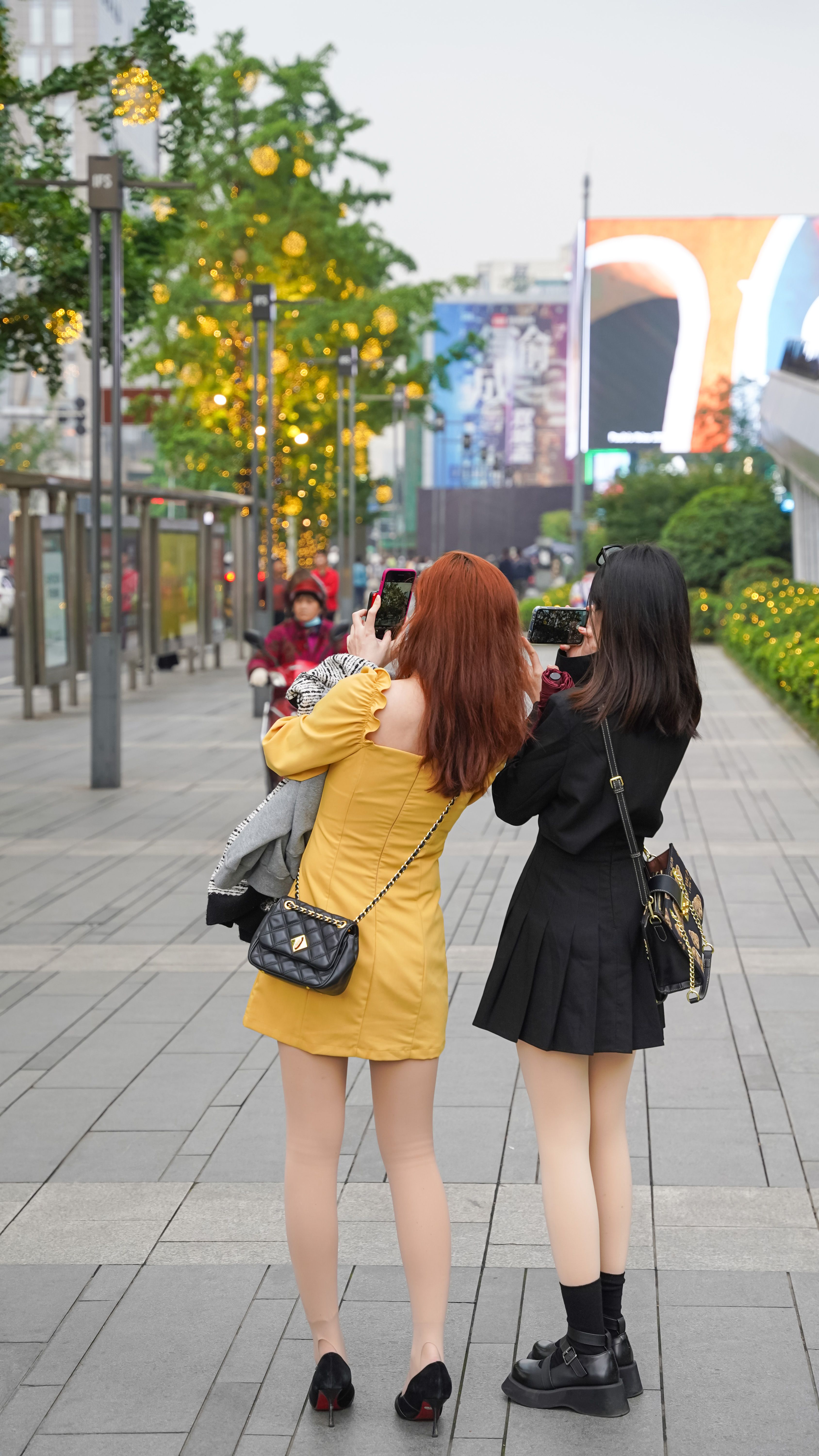 Two women photographing an urban street, capturing city life and architecture.