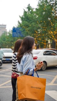 Two women with shopping bags on a city street crossing, bright day.