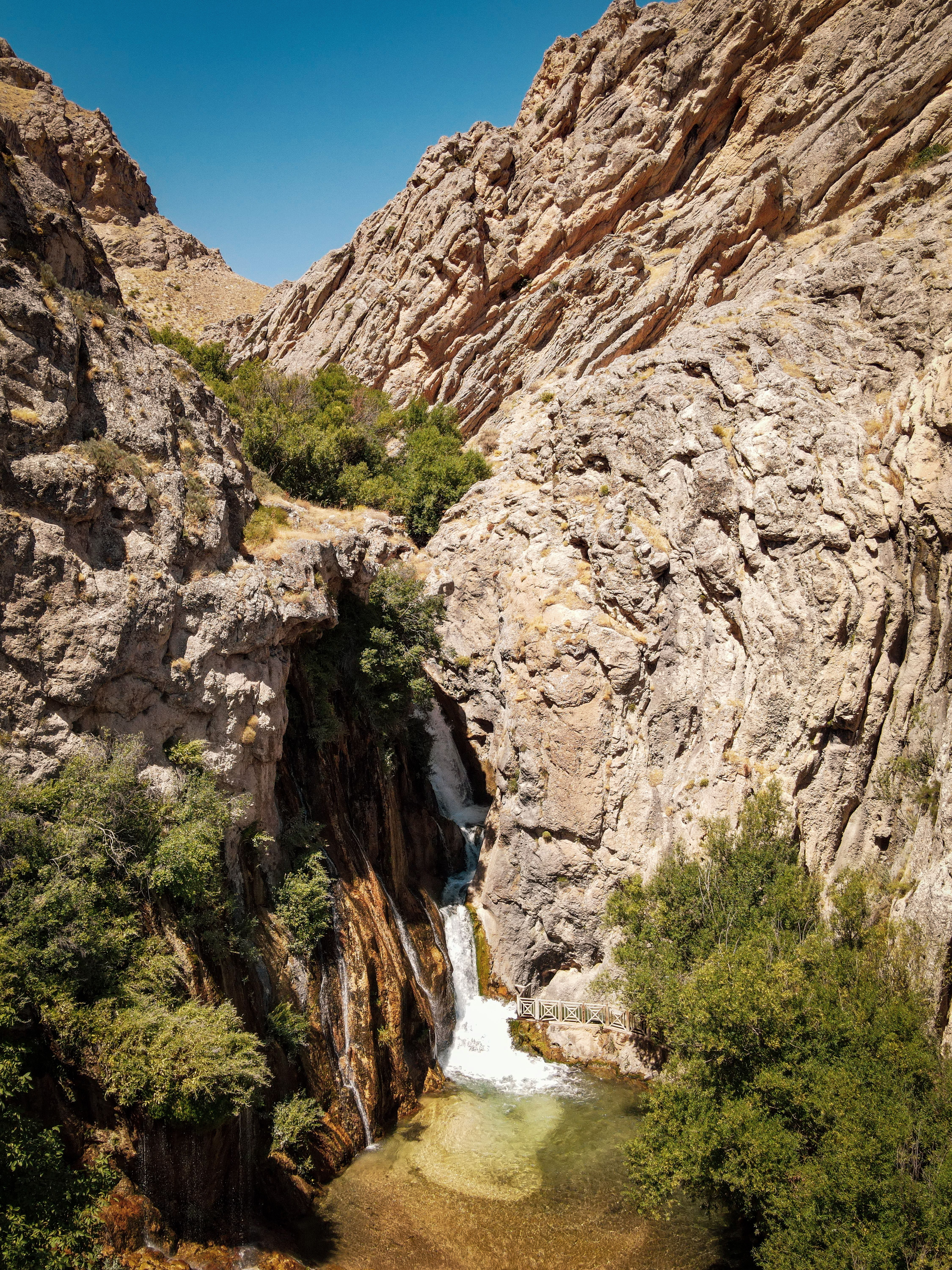A scenic waterfall cascades amidst eroded rocky cliffs under a clear sky.