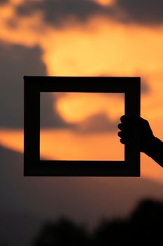 Silhouette of a hand holding a frame against a vibrant sunset sky.