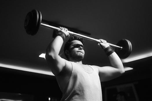 Black and white photo of a muscular man weightlifting indoors, showing strength and determination.