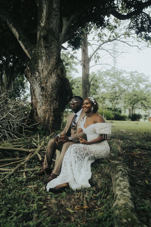 Free Charming African bride and groom sitting by a tree in a serene park setting. Stock Photo