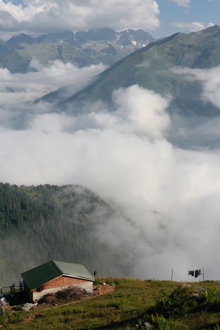 A picturesque mountain landscape features a solitary cabin amidst clouds, offering a tranquil rural scenery.