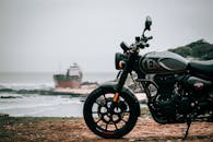 皇家恩菲尔德亨特350摩托车停泊在海边，旁边是一艘帆船