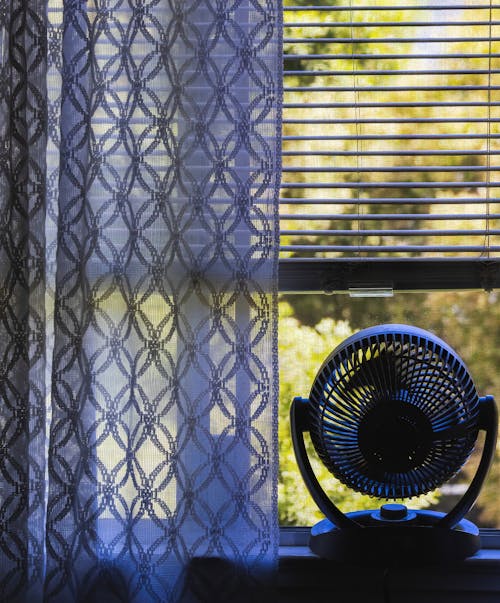 Window with a Patterned Curtain and a Fan on the Windowsill