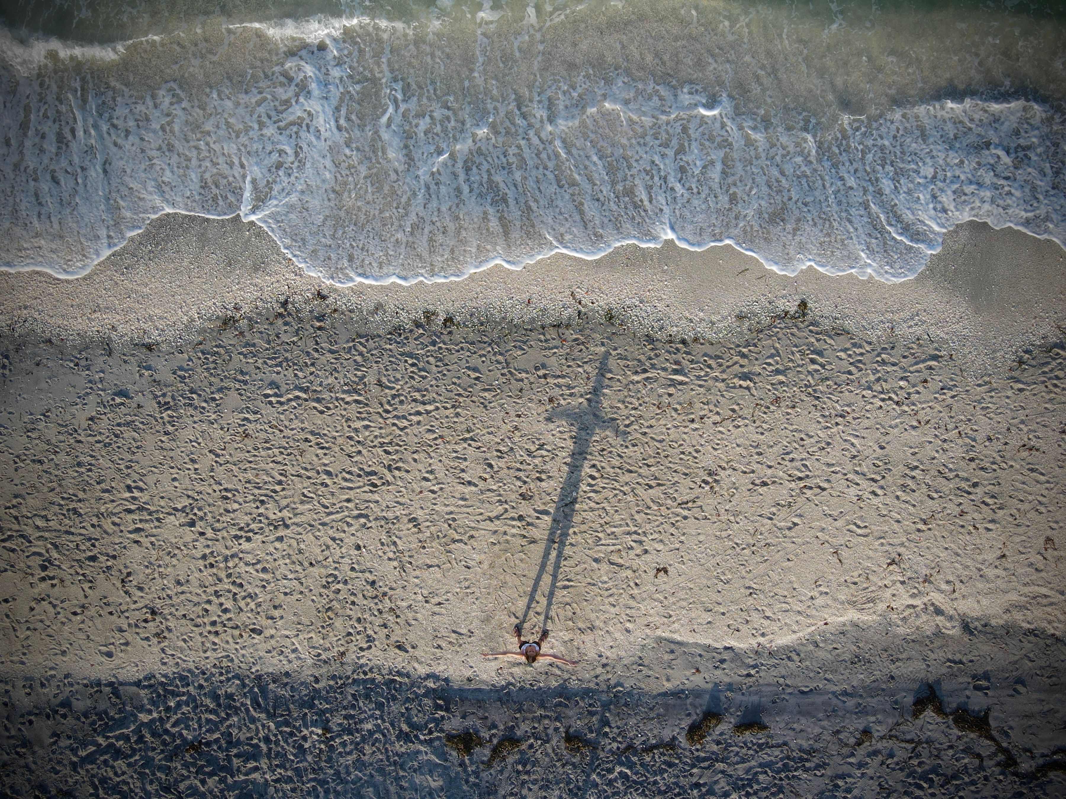 Drone shot of a person standing on Englewood beach with a long shadow and waves crashing on the shore.
