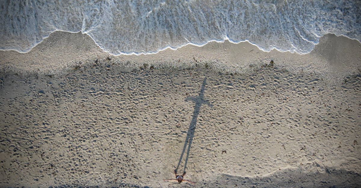 Drone shot of a person standing on Englewood beach with a long shadow and waves crashing on the shore.