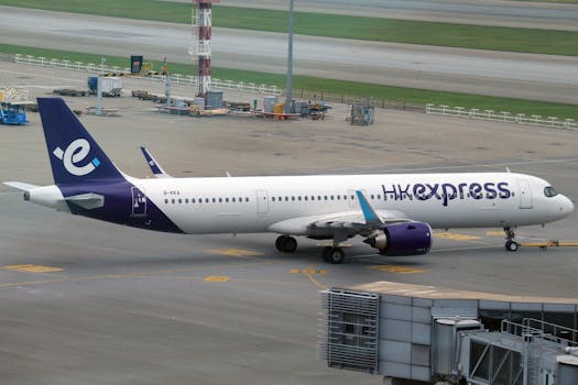 HK Express aircraft taxiing at an airport runway early in the day.