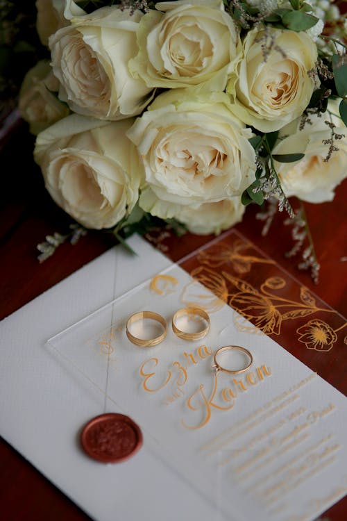 Wedding Rings and White Roses Bouquet Lying on a Table