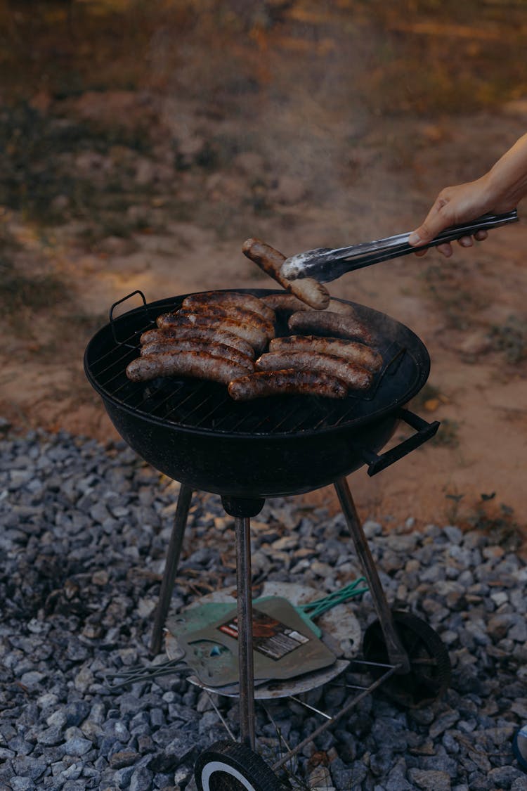 A Person Flipping Sausages On The Grill 